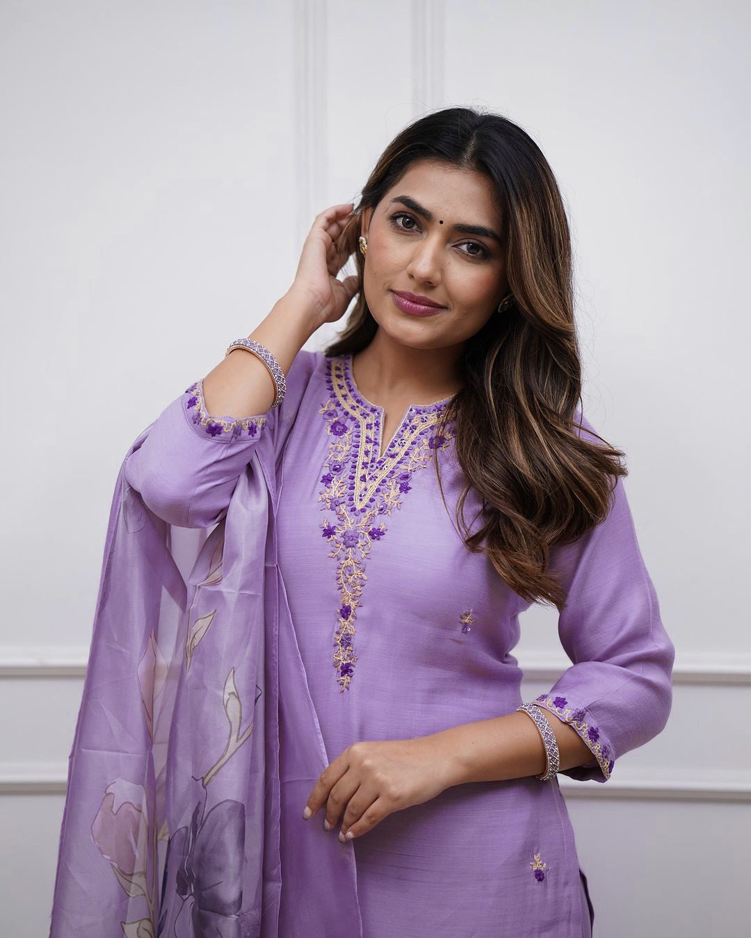 Close-up of a person wearing a purple outfit with embroidered details on a plain background